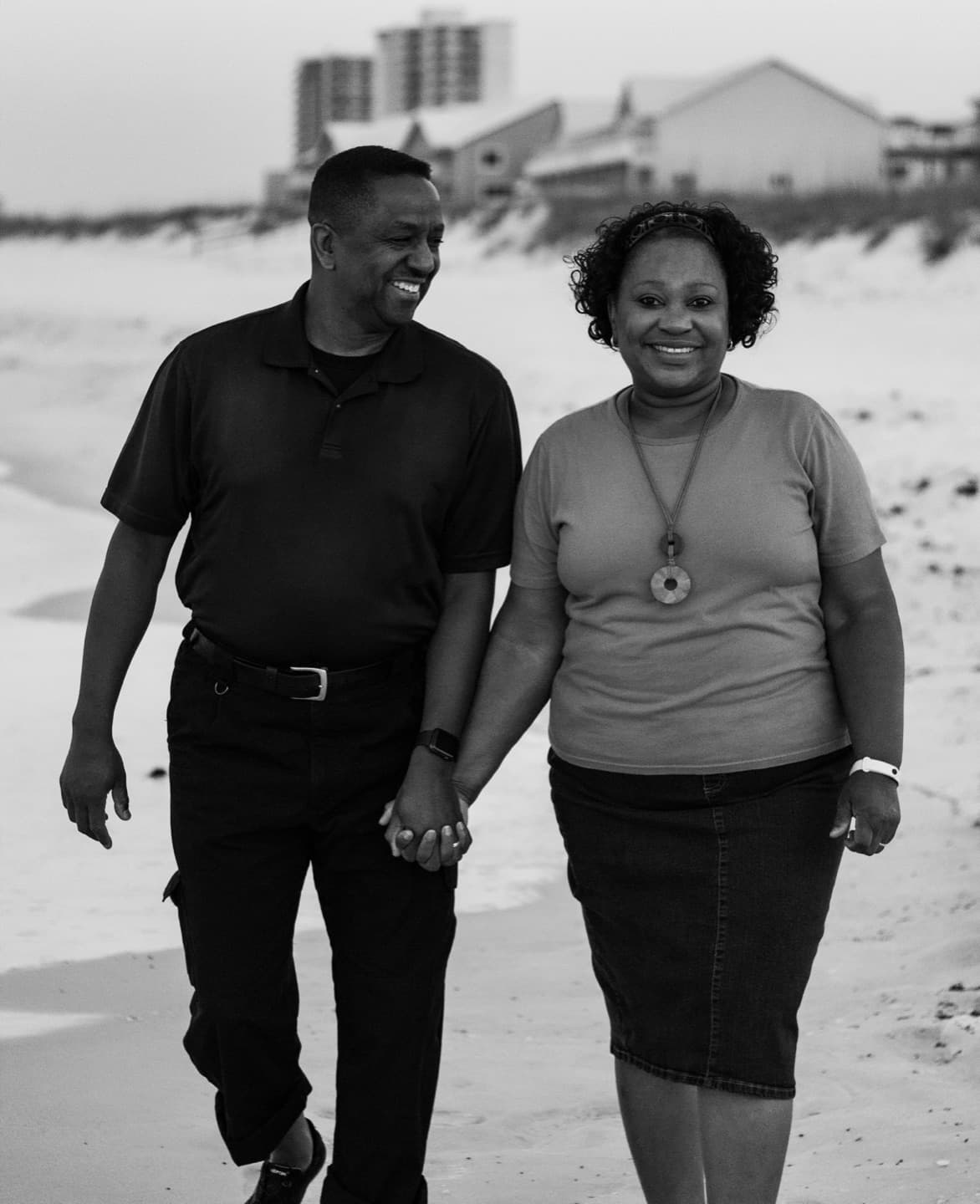A couple walking hand in hand along the beach in black and white