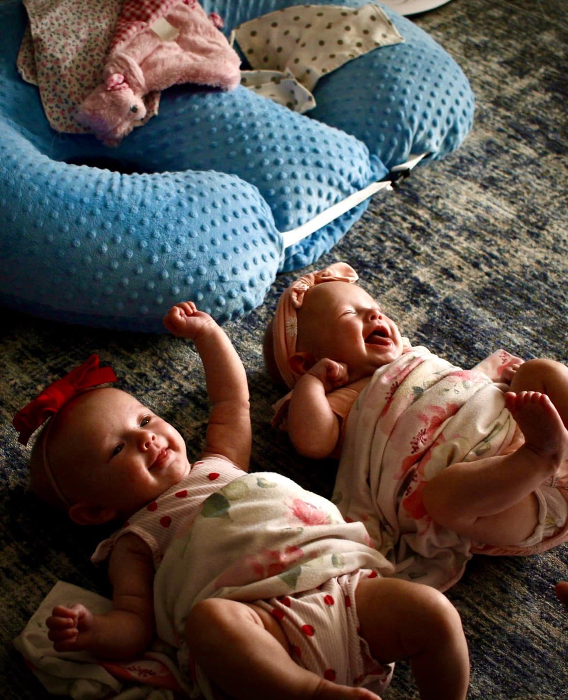 Two baby sisters lying on the floor, one laughing, one mid-yawn