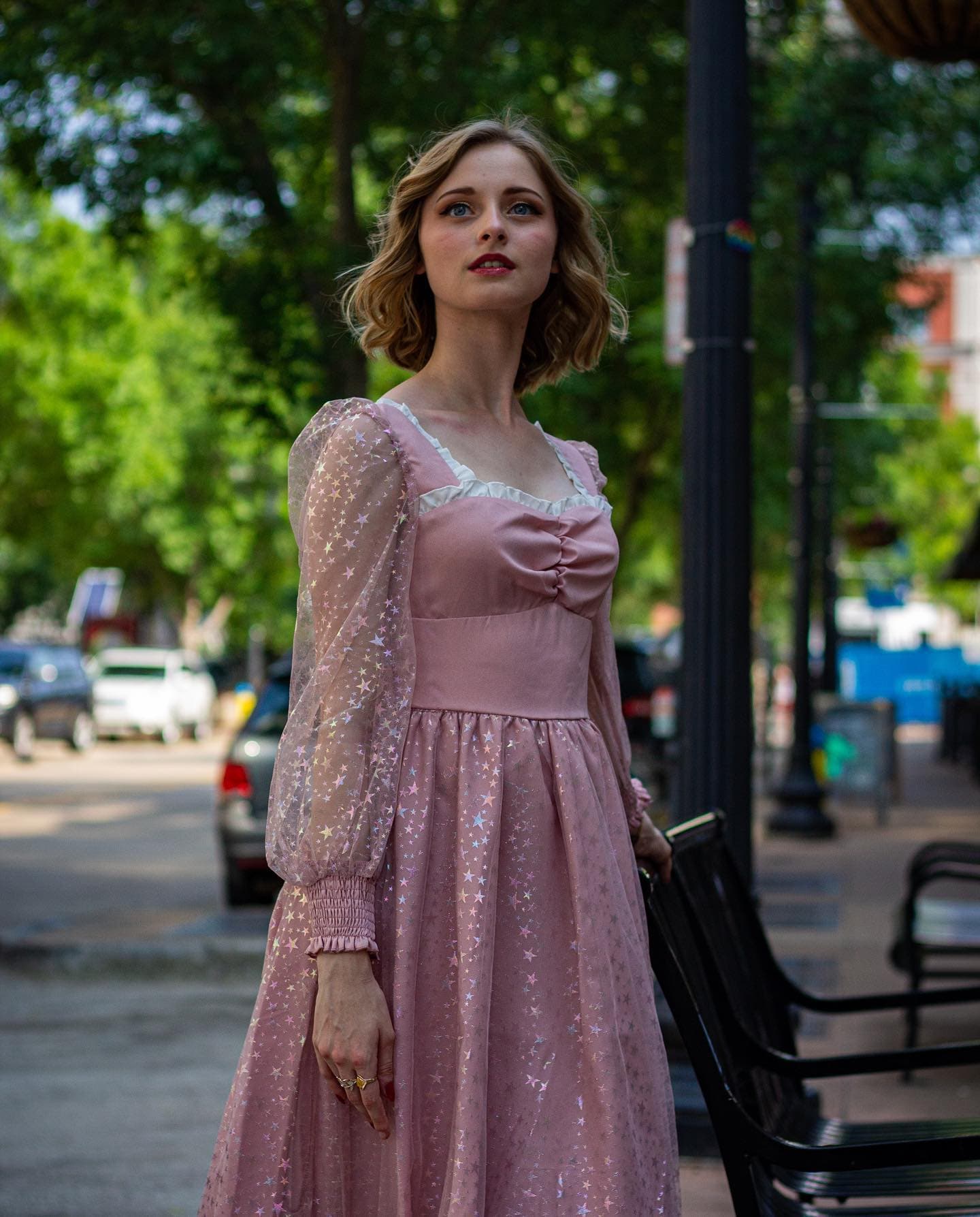 A young woman in a pink star-print dress on a downtown sidewalk