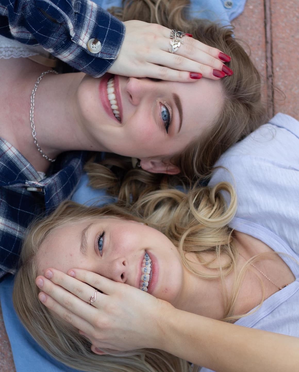 Two friends lying side by side, each covering the other's eyes